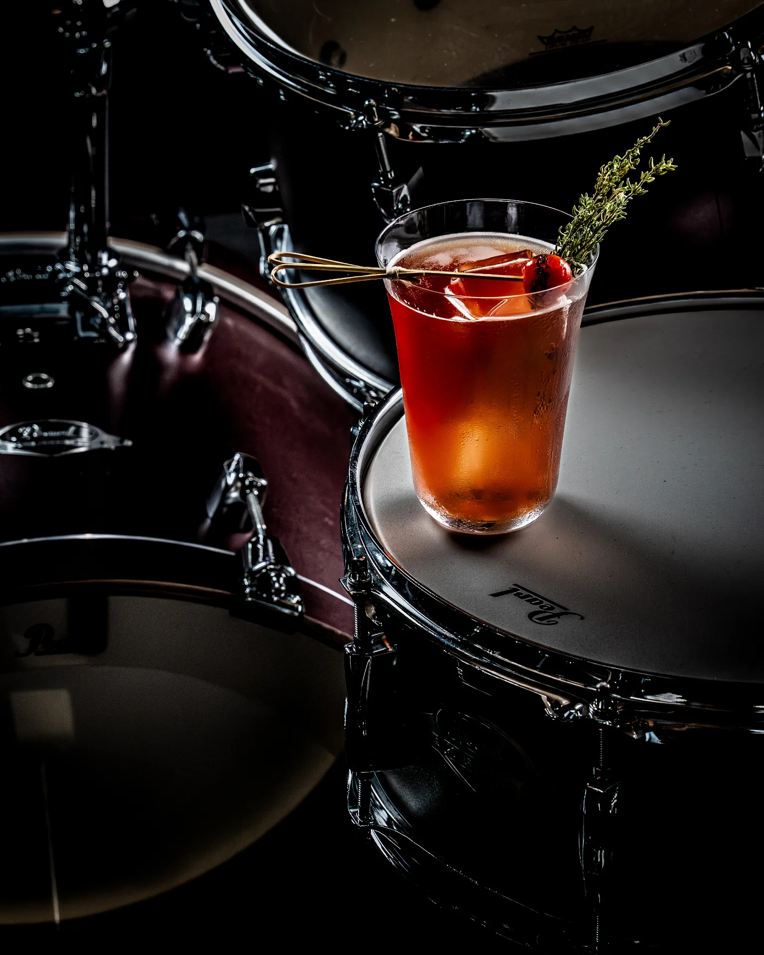 Cocktail garnished with thyme resting on a drum kit