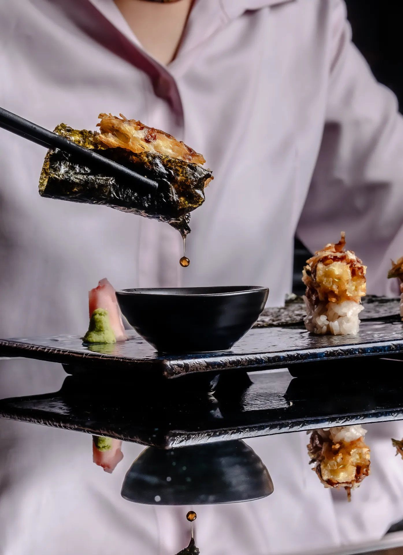 Tempura sushi being dipped into soy sauce with chopsticks