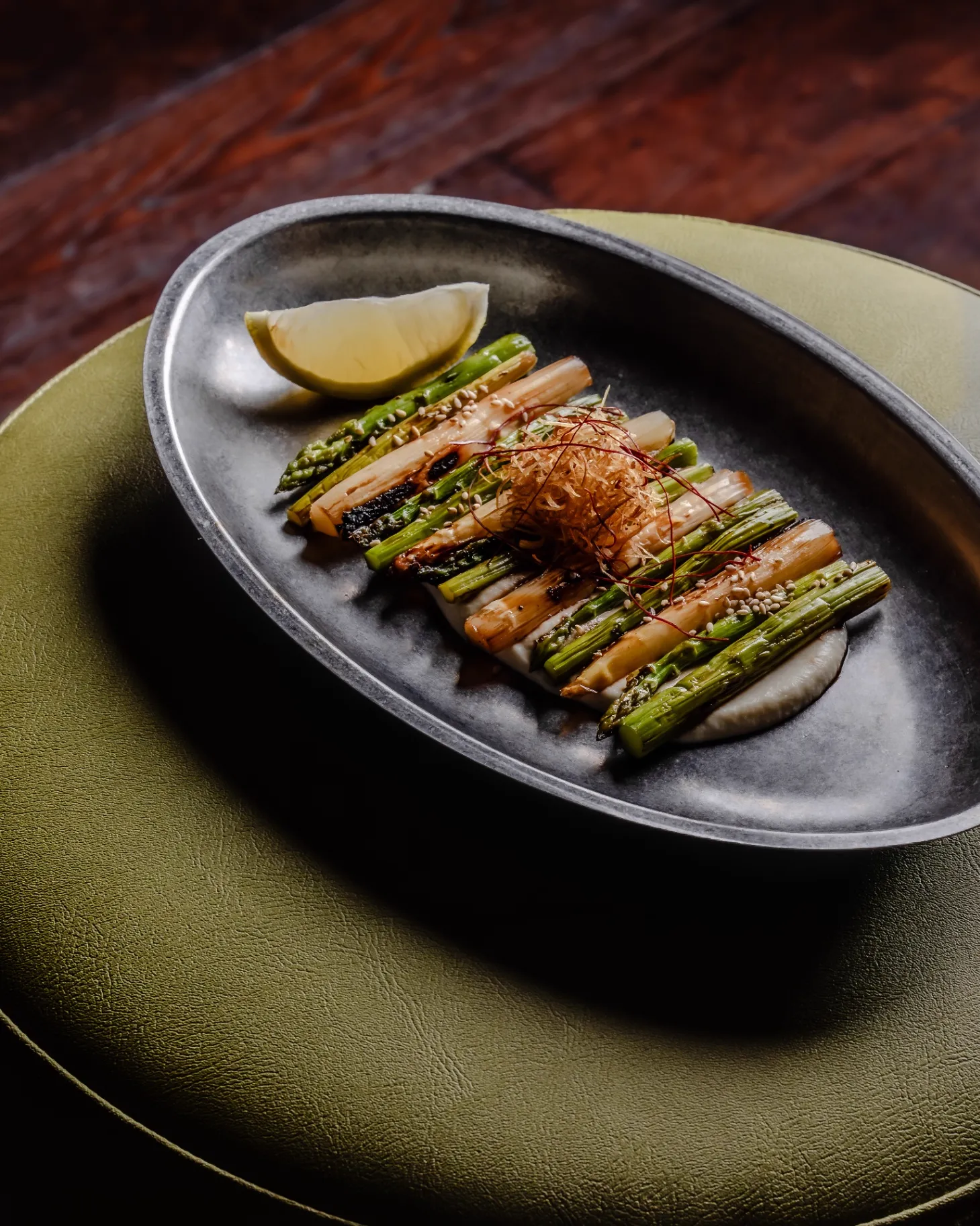 Charred asparagus and leeks with bonito flakes on a pewter dish