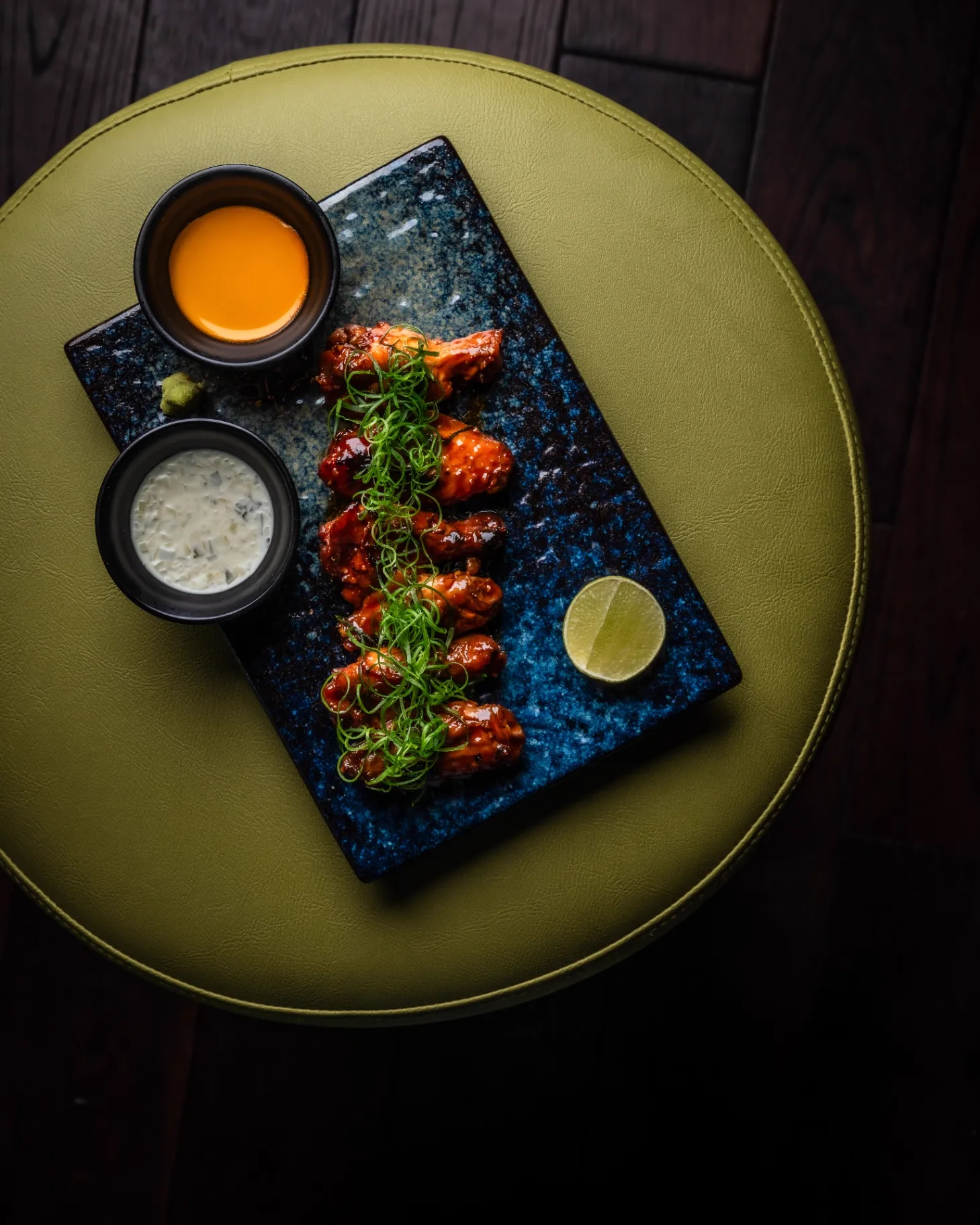 Glazed chicken wings with scallions and dipping sauces on a blue ceramic plate