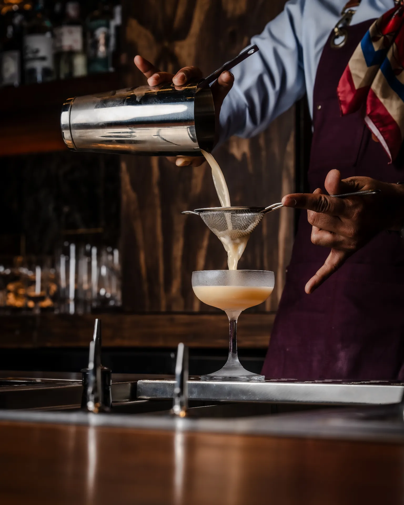 Bartender straining a cocktail into a frosted coupe