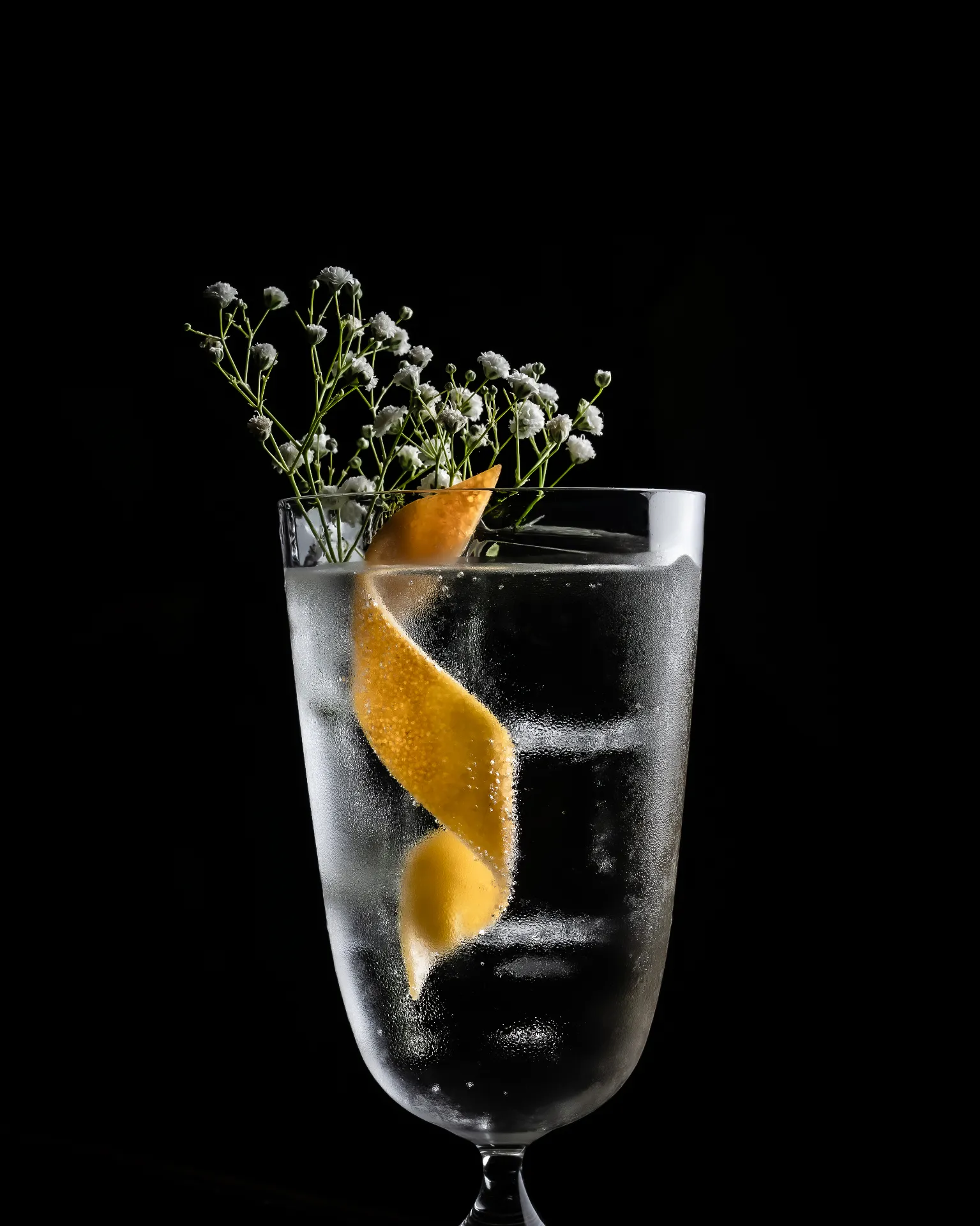 Clear citrus cocktail in a frosted highball glass against a black background